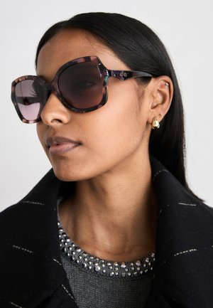 Üks suurte päikeseprillide paar, millel on kilpkonnakuju muster, tumedad objektiivid ja geomeetrilised raami. Kandmisel musta jope ja kaunistatud kaelusega.