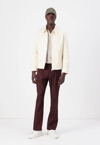 Biała pikowana kurtka, textured lekki sweter, burgundowe spodnie i białe sneakersy. W komplecie z oliwkową czapką.