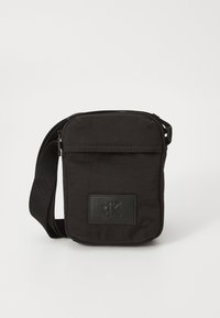 Borsa a tracolla in tessuto nero con chiusura con zip, tasca frontale e accent in pelle con il logo "cK". Inclusa tracolla regolabile.