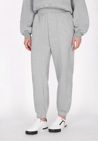 Grå sweatpants lavet af blødt stof; elastisk talje og manchetter; parret med hvide sneakers med sorte accenter.