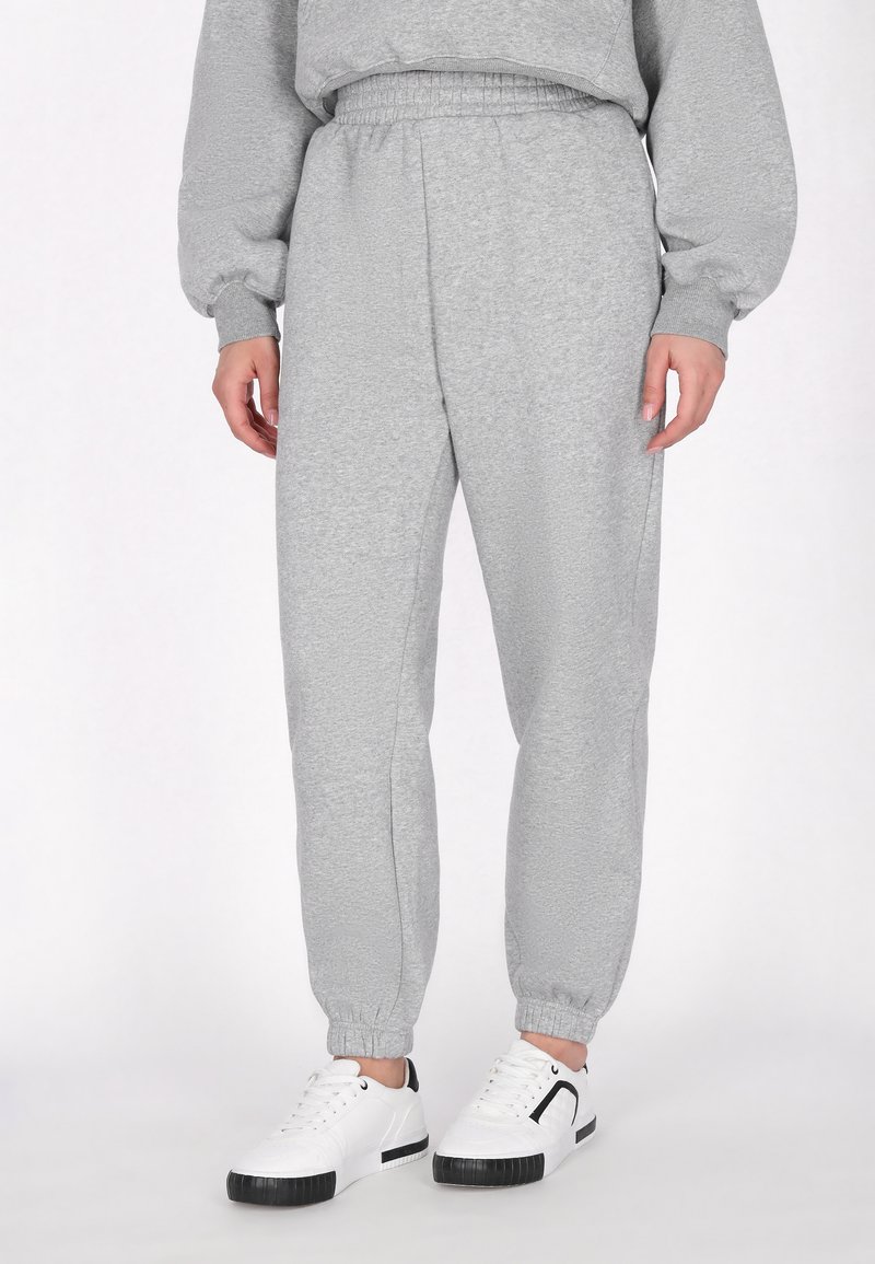 Grå sweatpants lavet af blødt stof; elastisk talje og manchetter; parret med hvide sneakers med sorte accenter.