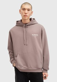 Lysebrun hoodie lavet af bomuld, med en frontlomme, justerbare snoretræk og et hvidt logo printet på brystet.