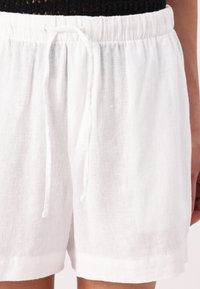 Pantalones cortos de lino blanco con cintura elástica, que presentan un ajuste relajado y una textura suave. El dobladillo está terminado con un corte recto.