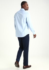 Camisa de manga larga de color azul claro con cuello abotonado, combinada con pantalones oscuros de color navy, mostrando un ajuste casual y una textura de tela suave.