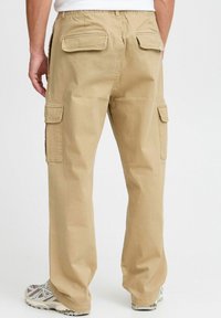 Beige cargobroeken gemaakt van katoen, met achter- en zijzakken, een losse pasvorm en een eenvoudig design van de tailleband. Draag met grijze sneakers.