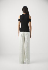 Musta kylmä-hartiainen paita, jossa on tiukka muotoilu, yhdistettynä väljät vaaleanbeigeet housut, joilla on sileä pinta ja minimaalinen yksityiskohtaisuus.