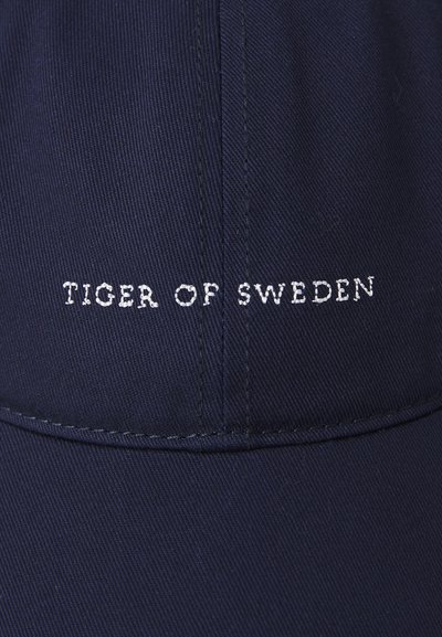 Merineitsi müts, mis on valmistatud tekstuuritud kangast, mille esipoolt kaunistab valge niidiga broderitud "TIGER OF SWEDEN" logo.