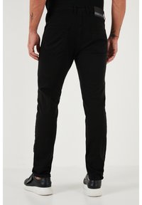 Fekete farmernadrág, slim fit szabásban, sima textúrával, standard zsebekkel és szürke márkás folttal a derékrészen.
