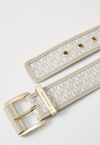 Cintura in tessuto beige con un motivo testurizzato, fibbia in metallo dorato e occhielli. Presenta uno spesso retro in ecopelle e dettagli in cucitura.