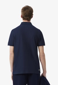 Marinblå pikétröja med korta ärmar, texturerad tyg och krage. Har en liten grön logotyp nederst till vänster.