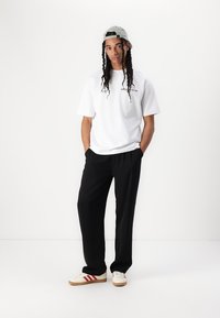 White short-sleeve T-shirt with "DON'T BUY CULTURE" text, black loose-fit trousers, and cream sneakers with red stripes and tan soles.
