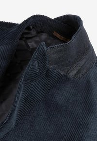 Dark navy corduroy fabric with prominent ribbed texture. Features a lined collar with a subtle sheen and a black checkered inner lining.