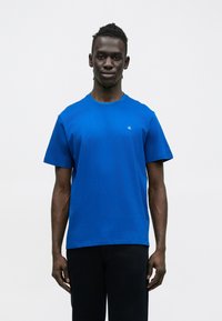 Koszulka w kolorze królewskiego niebieskiego wykonana z bawełny, z okrągłym dekoltem i krótkimi rękawami. Subtelne logo na wysokości klatki piersiowej.