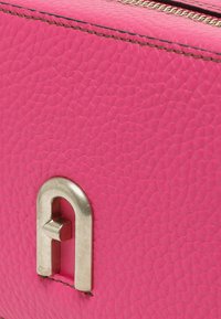 Borsa in pelle strutturata rosa con una chiusura metallica caratterizzata da un design astratto. I dettagli delle cuciture lungo il bordo ne esaltano la struttura.