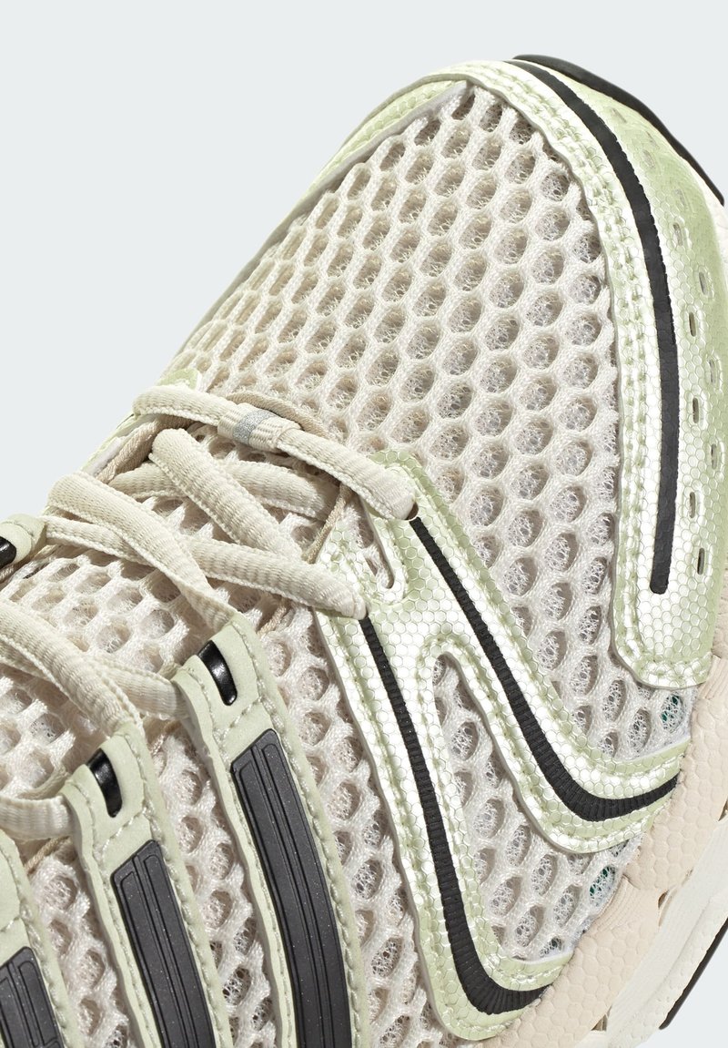 Leichtgewichtiger Sportschuh mit einem atmungsaktiven Mesh-Obermaterial in Beige mit grünen Akzenten, schwarzen Streifen und einer strukturierten Dämpfungssohle.