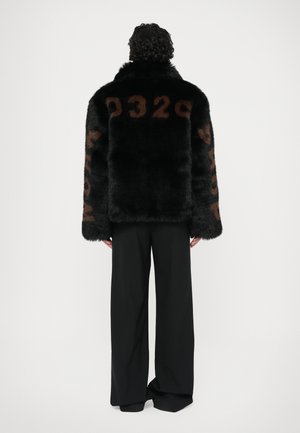 Schwarze Kunstfelljacke mit großen braunen numerischen Details auf dem Rücken und den Ärmeln, kombiniert mit schwarzen weit geschnittenen Hosen.