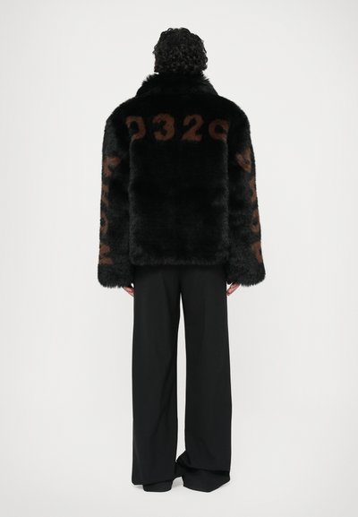 Schwarze Kunstfelljacke mit großen braunen numerischen Details auf dem Rücken und den Ärmeln, kombiniert mit schwarzen weit geschnittenen Hosen.