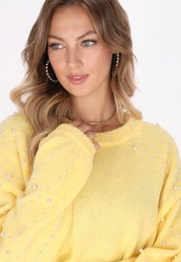 Pulover tricotat de culoare galben deschis, cu guler cu nervuri, embellishments cu perle pe mâneci și textură moale.