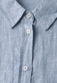 Lichtblauw linnenshirt met een kraag, voorzien van twee witte knopen aan de voorkant en een gestructureerd stofoppervlak.