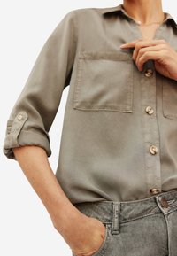 Lichtgrijs overhemd met lange mouwen, met twee borstzakken en een gladde stofstructuur, gecombineerd met denim broek.