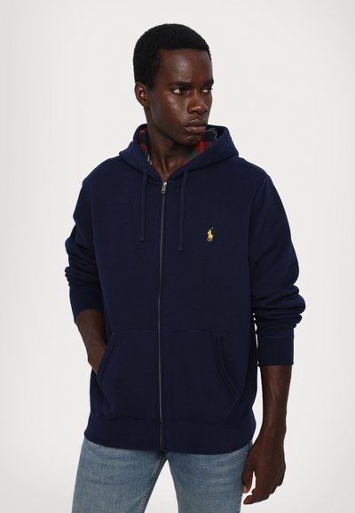 Sweat-shirt à capuche zippé bleu marine avec une poche avant et un logo brodé. Doublé en tissu tartan, avec des poignets et un ourlet côtelés.