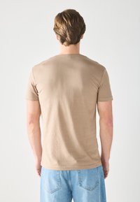 Camiseta de manga corta en beige, hecha de una tela suave, con un cuello redondo y un dobladillo recto, combinada con pantalones cortos de mezclilla azul claro.