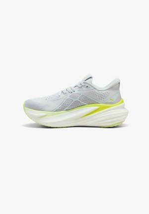 Zapatilla de correr gris claro con parte superior de malla, detalles en amarillo, entresuela gruesa blanca y suela exterior texturizada para mayor agarre. Cuenta con cordones y cuello acolchado.