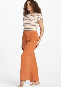 Striped crop top in white and orange, paired with loose, textured orange pants featuring an elastic waistband and wide leg design.