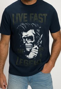 Mörkblå bomulls t-shirt med en grafik av ett skeptiskt huvud med hår och en kniv, text med "LEVA SNABBT DÖ SOM EN LEGEND" i sliten gul.