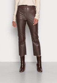 Pantalon en simili cuir marron à texture lisse, taille haute et longueur raccourcie, associé à des bottes à talons marron brillant avec un détail zippé.
