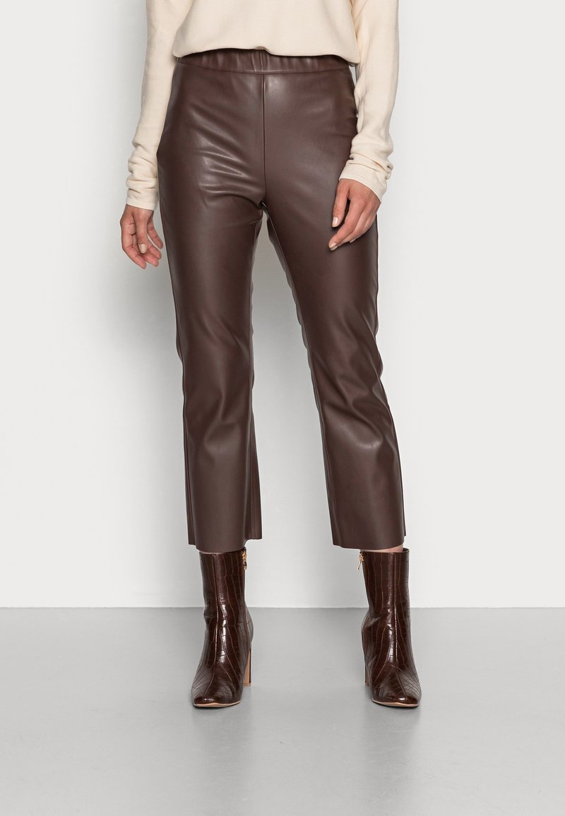 Pantalon en simili cuir marron à texture lisse, taille haute et longueur raccourcie, associé à des bottes à talons marron brillant avec un détail zippé.