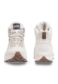 Světlé krémové turistické boty s texturovaným svrškem, polstrovaným límcem a gumovými podrážkami s výrazným vzorem pro grip.
