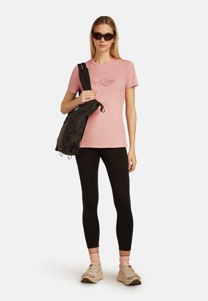 Camiseta de algodón rosa con un estampado gráfico, bolso cruzado negro, leggings negros y zapatillas beiges. Las gafas de sol completan el conjunto.