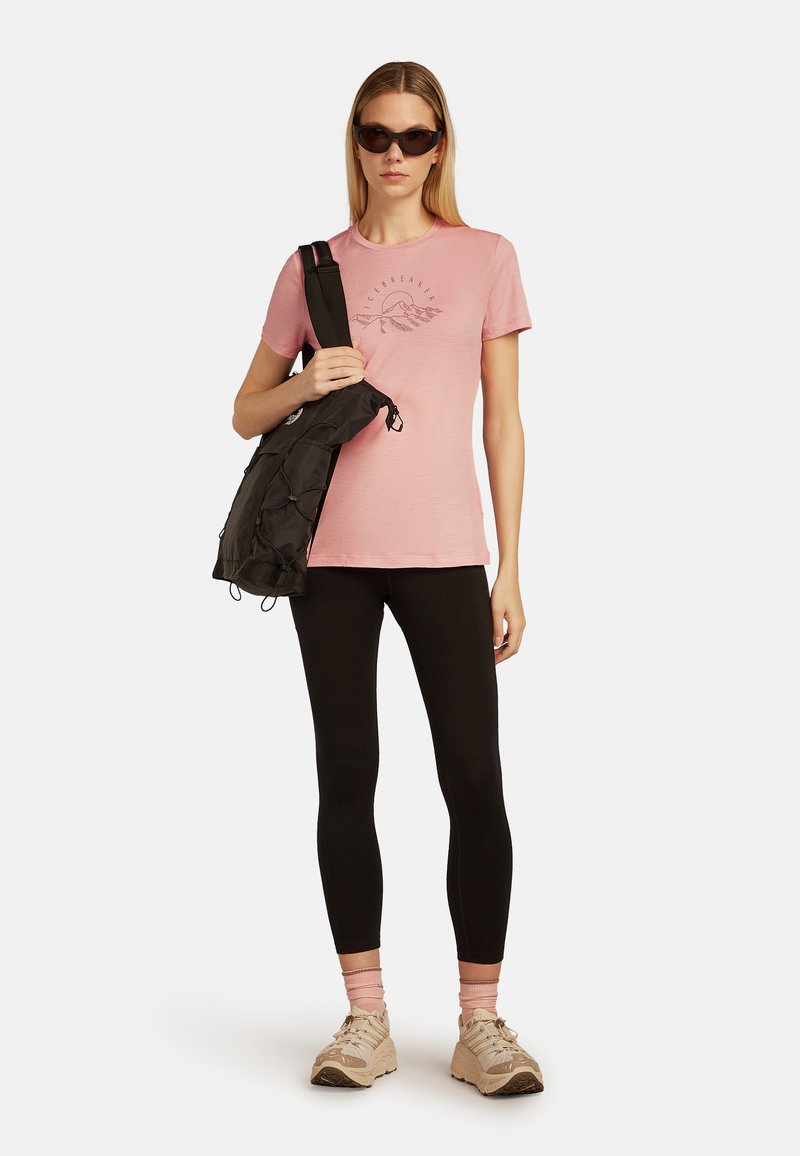 Rosa bomullströja med grafiskt tryck, svart axelväska, svarta leggings och beige sneakers. Solglasögon fulländar outfiten.