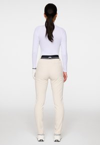 Valkoinen pitkähihaista puseroa yhdistettynä vaaleanbeigeihin istuviin housuihin, joissa on musta vyötärönauha. Lisätietona on myös hansikas vasemmassa kädessä.