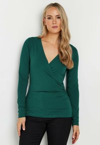 Langärmlige, tiefgrüne Wickelbluse aus weichem Stoff, mit V-Ausschnitt und gerafftem Detail an der Taille für eine figurbetonte Passform.