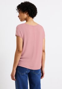 Růžový top s krátkým rukávem a volným střihem, s kulatým výstřihem a hladkou texturou, zkombinovaný s modrými džíny s zadními kapsami.