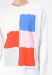 Hosszú ujjú fehér ing, amely négy színblokk grafikai mintázatával rendelkezik: piros, kék, rózsaszín és szürke, textúrált ecsetvonás effektussal.