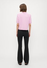 Polo shirt rosa chiaro a maniche corte con colletto, design accorciato e texture sottile, abbinato a pantaloni neri a vita alta e svasati.