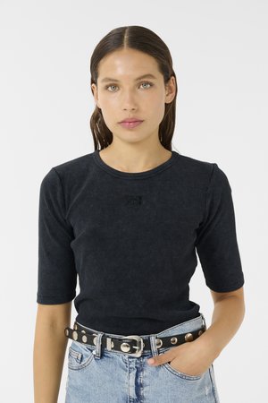 Svart ribbet topp med korte ermer og rund halslinning, med en subtil logo detalj; brukt med høyhælte lyseblå jeans og et svart belte med sølvnitter.