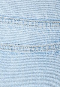 Helle blaue Denim-Stoff mit zwei parallel genähten Nähten, die horizontal über den Stoff verlaufen.