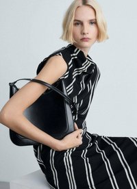 Sac en cuir noir de forme triangulaire avec une seule sangle, tenu par un modèle portant une robe à rayures noir et blanc. Texture lisse.