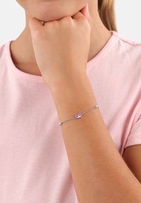 Silberne Kettenarmband mit einem kleinen Blumenmuster und rosa Akzenten, das an einem Handgelenk auf einem hellrosa Hemd-Hintergrund getragen wird.
