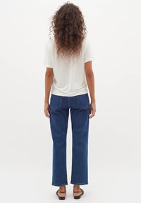 Vit kortärmad t-shirt kombinerad med blå raka jeans. Tyget verkar mjukt, med subtila sömnadsdetaljer och en avslappnad passform.