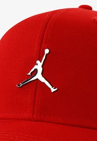 Sarkans beisbola cepure, izgatavota no teksturēta auduma, ar sudraba Jumpman logo uz priekšējā paneļa. Izliekta vainaga struktūra ar ieliektu vizoru.