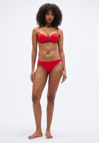 Σετ κόκκινου μπικίνι που περιλαμβάνει σουτιέν με στρίψιμο στο μπροστινό μέρος και ρυθμιζόμενους ιμάντες, καθώς και ένα σλιπ με χαμηλή μέση. Λείο ύφασμα με εφαρμοστή σχεδίαση.