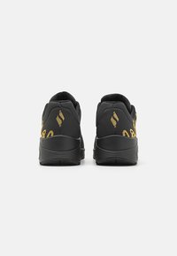 Scarpe da ginnastica nere con dettagli dorati, caratterizzate da un design elegante, colletto imbottito e suole testurizzate. Logo e motivo ben visibili sui lati.