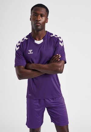 T-shirt de sport violet à manches courtes avec des accents blancs, associé à un short violet. Présente un logo sur la poitrine et des bandes d'épaule contrastantes.
