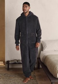 Salopetă din polar de culoare gri închis, cu mâneci lungi, glugă și închidere cu fermoar. Include buzunare frontale și manșete ribbate la încheieturi și glezne.