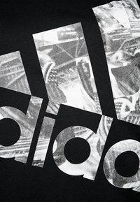 Černá tkanina s velkým bílým grafickým textem překrytým texturovaným vzorem, zobrazující logo a abstraktní motivy.